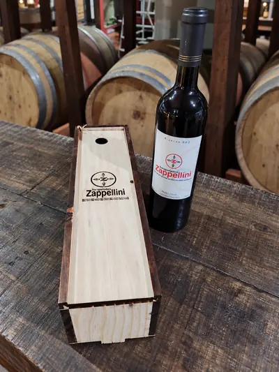 Garrafa de vinho com rótulo da Zappellini ao lado de caixa de madeira com o logo gravado